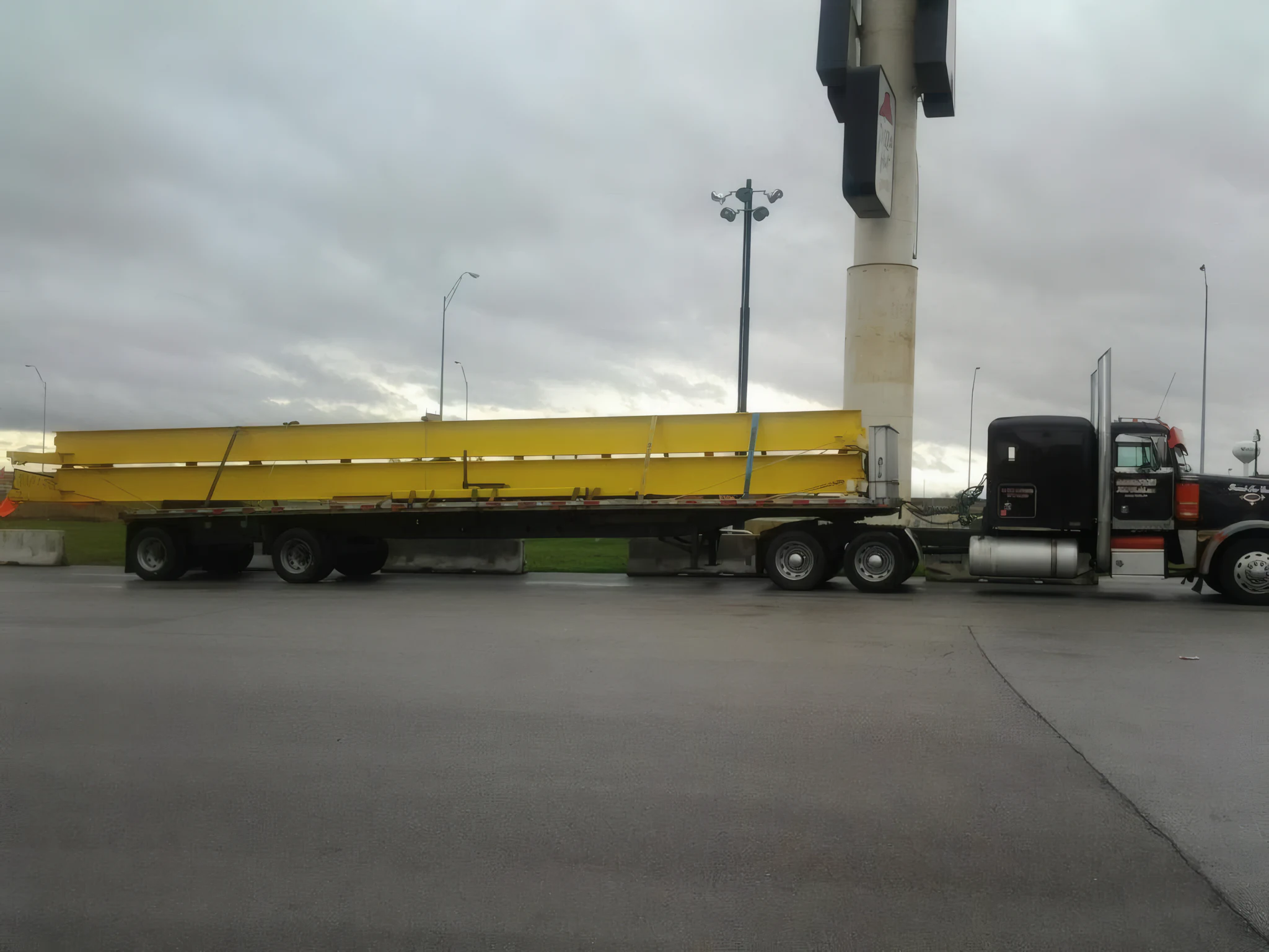 Structural steel beams strapped and blocked across a flatbed trailer behind a Peterbilt tractor