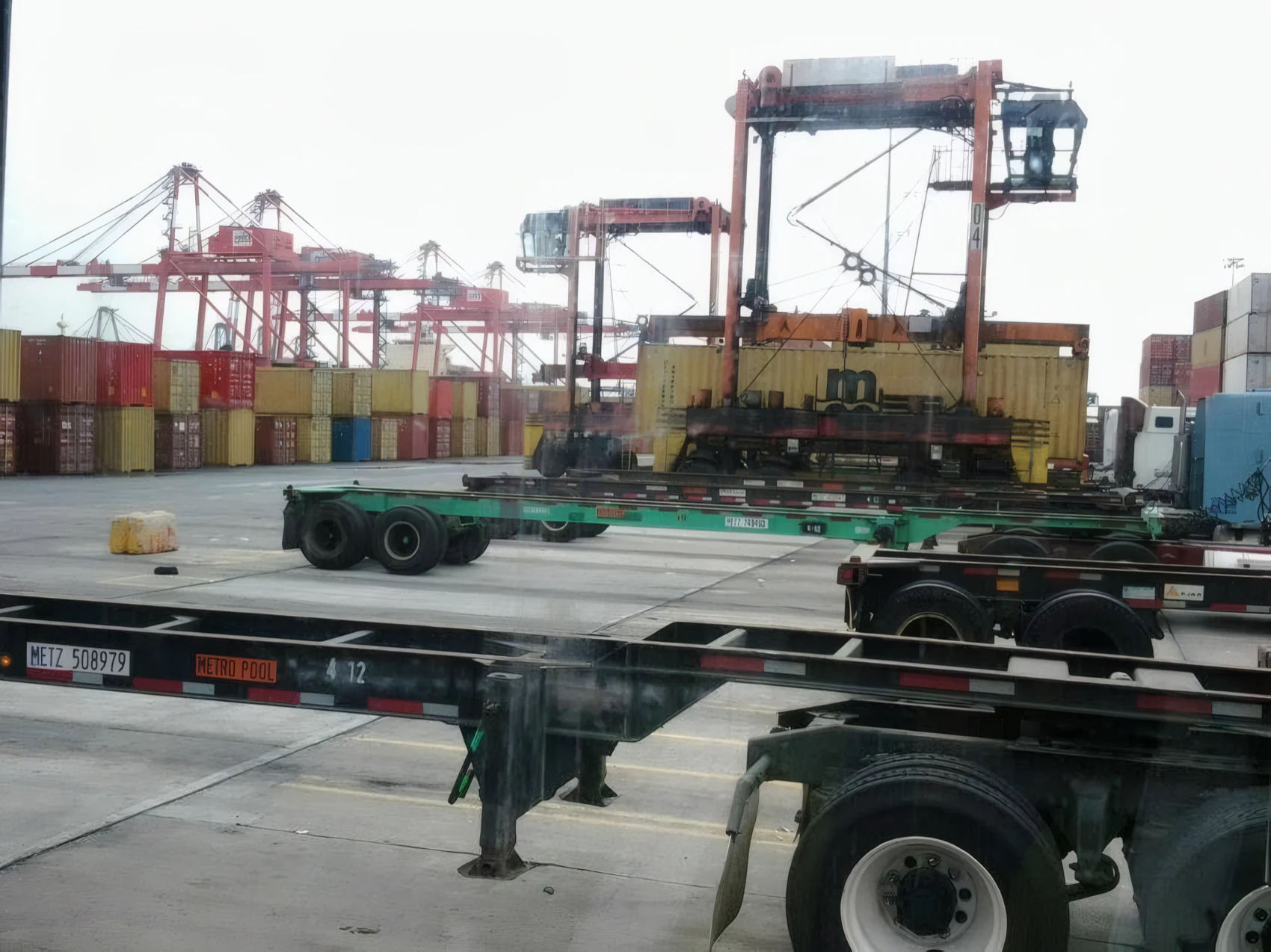Ship-to-shore gantry cranes and stacked containers behind a row of empty chassis inside a marine container terminal